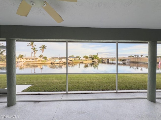 unfurnished sunroom featuring ceiling fan and a water view