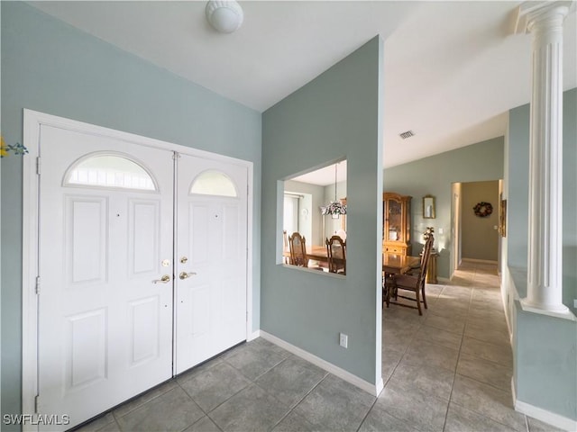 tiled foyer entrance with ornate columns, a chandelier, and lofted ceiling