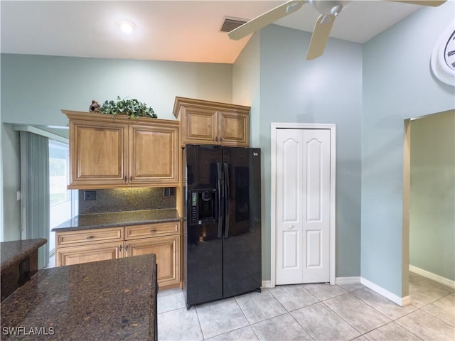 kitchen featuring backsplash, dark stone counters, black fridge, vaulted ceiling, and light tile patterned flooring