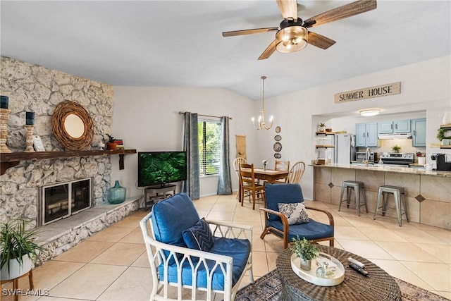 living room featuring a stone fireplace, ceiling fan with notable chandelier, light tile patterned floors, and vaulted ceiling