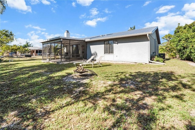 rear view of house featuring a fire pit, a lawn, and a sunroom