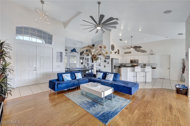 living room featuring high vaulted ceiling, ceiling fan with notable chandelier, and light hardwood / wood-style floors