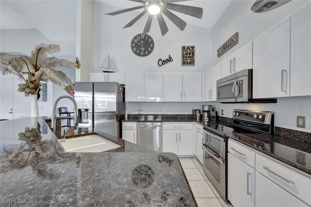 kitchen with sink, high vaulted ceiling, appliances with stainless steel finishes, dark stone counters, and white cabinets