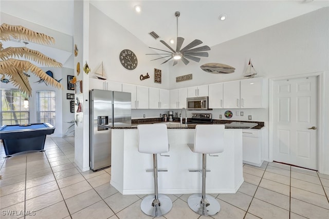 kitchen featuring a breakfast bar, white cabinetry, light tile patterned floors, appliances with stainless steel finishes, and a kitchen island with sink