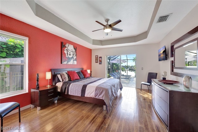 bedroom with a raised ceiling, ceiling fan, access to outside, and light wood-type flooring