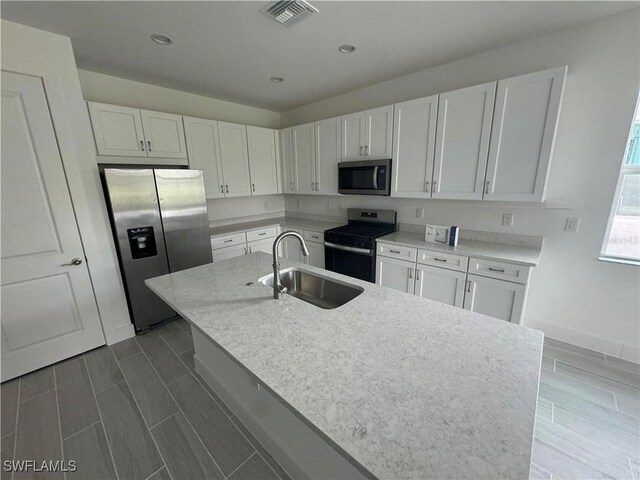 kitchen featuring white cabinets, sink, stainless steel appliances, and a kitchen island with sink