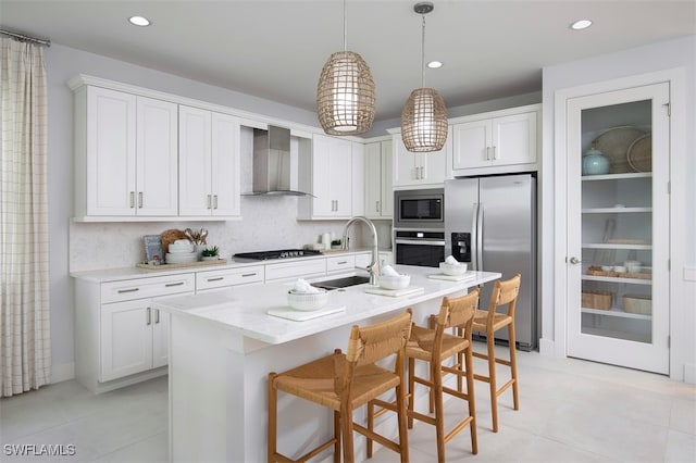 kitchen featuring a breakfast bar area, appliances with stainless steel finishes, hanging light fixtures, wall chimney range hood, and a sink