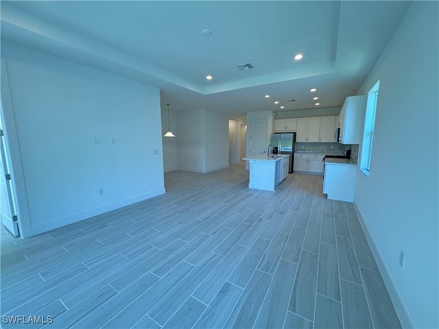 kitchen with visible vents, white cabinets, open floor plan, a raised ceiling, and a center island with sink