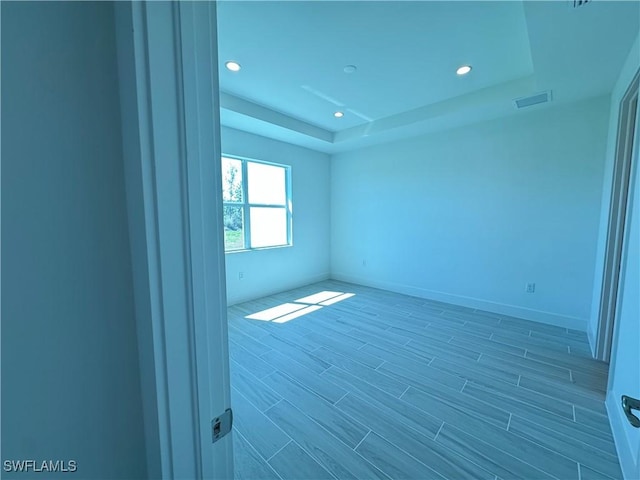 unfurnished room featuring baseboards, visible vents, wood finished floors, a tray ceiling, and recessed lighting