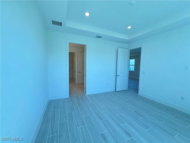 unfurnished bedroom with a tray ceiling, visible vents, and light wood-style floors