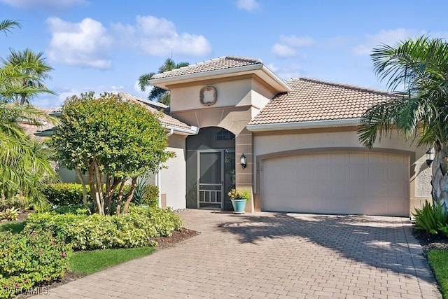 mediterranean / spanish home featuring a tiled roof, decorative driveway, a garage, and stucco siding