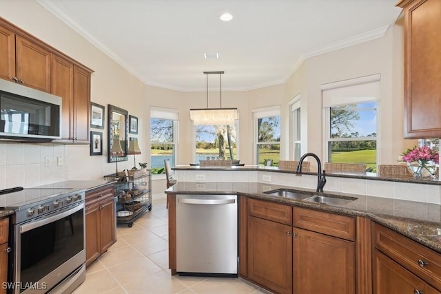 kitchen with appliances with stainless steel finishes, dark stone counters, crown molding, sink, and decorative light fixtures