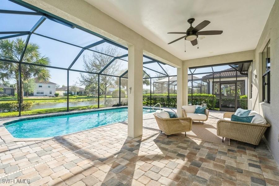 view of pool featuring a patio area, a water view, glass enclosure, outdoor lounge area, and ceiling fan