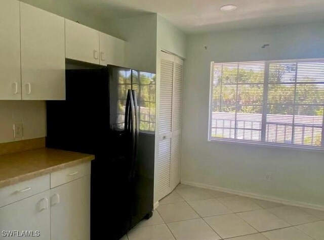 kitchen featuring white cabinets, light tile patterned floors, and black refrigerator