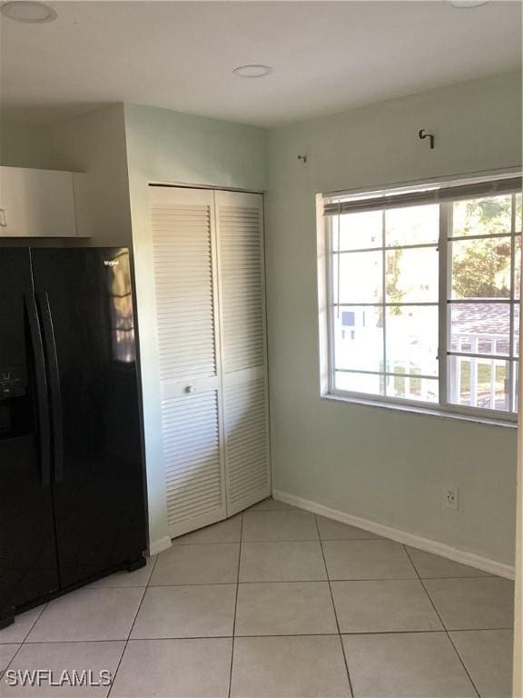 unfurnished bedroom featuring light tile patterned flooring, black fridge, and a closet