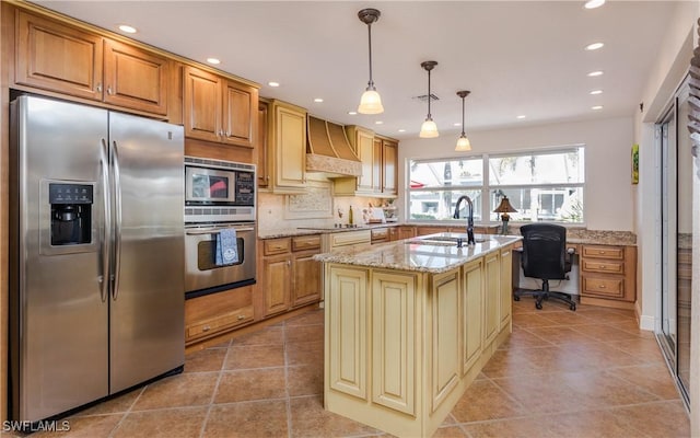 kitchen with light stone countertops, premium range hood, stainless steel appliances, sink, and a center island with sink