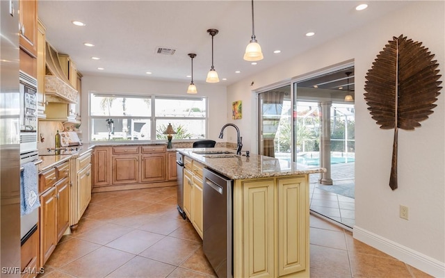 kitchen with sink, light stone countertops, an island with sink, light tile patterned floors, and decorative light fixtures