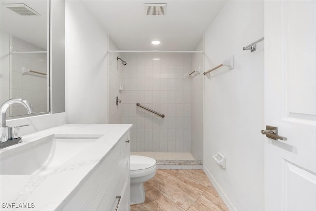 bathroom with a tile shower, vanity, and toilet