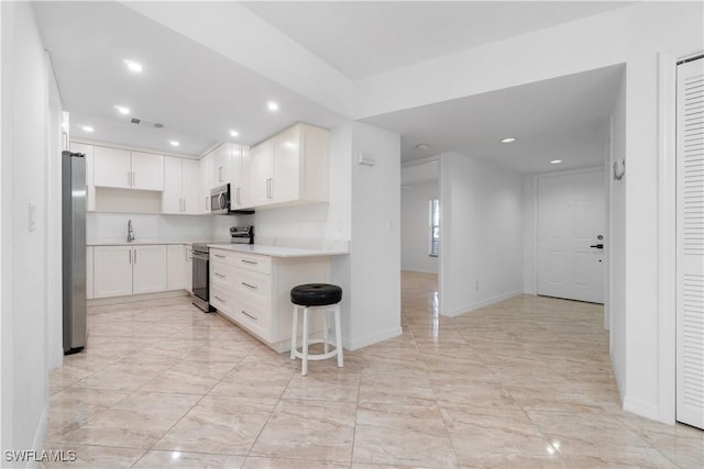 kitchen featuring a kitchen bar, white cabinetry, sink, and appliances with stainless steel finishes