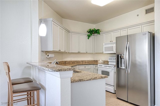 kitchen with white appliances, stone counters, kitchen peninsula, a kitchen bar, and white cabinetry