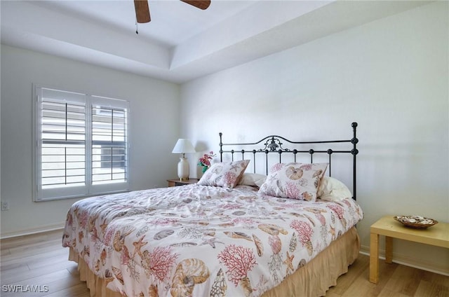 bedroom featuring ceiling fan, a tray ceiling, and light hardwood / wood-style flooring