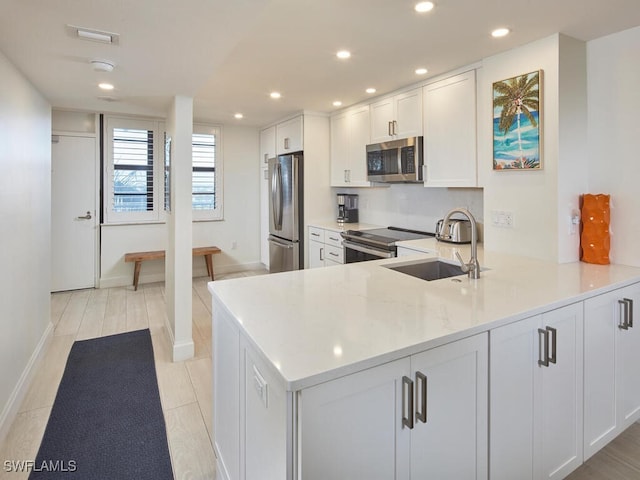 kitchen with light stone countertops, sink, stainless steel appliances, kitchen peninsula, and white cabinets