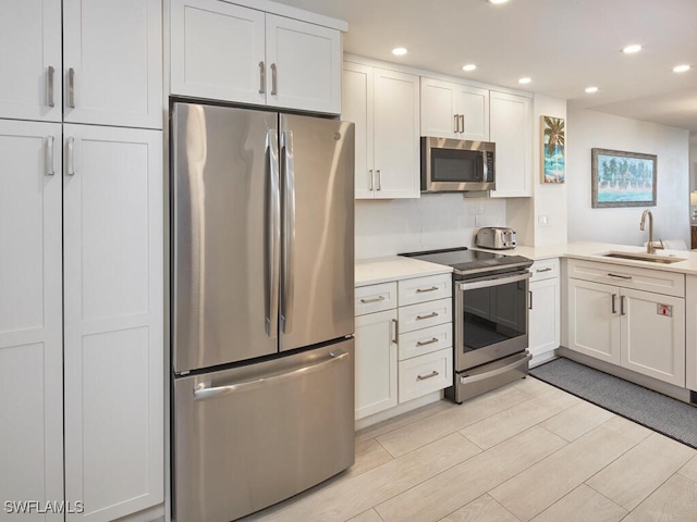 kitchen with stainless steel appliances, white cabinetry, light hardwood / wood-style floors, and sink