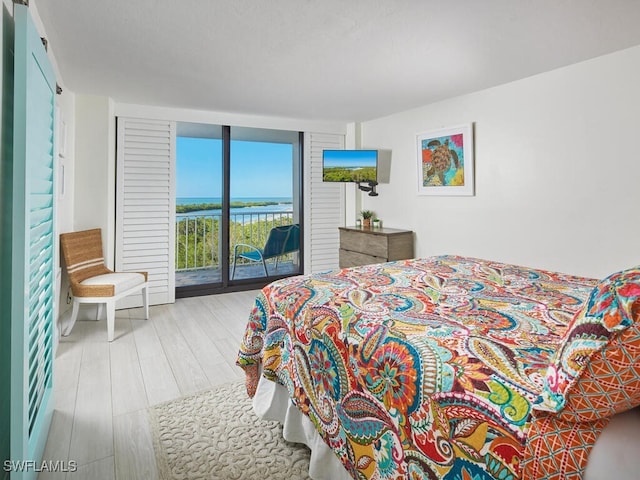 bedroom featuring access to exterior, expansive windows, and light wood-type flooring