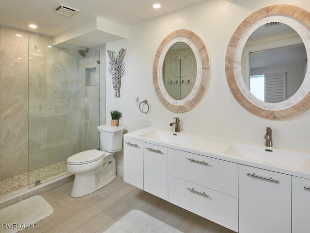 bathroom with hardwood / wood-style floors, vanity, toilet, and a tile shower