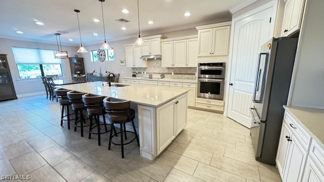 kitchen with hanging light fixtures, sink, an island with sink, appliances with stainless steel finishes, and tasteful backsplash