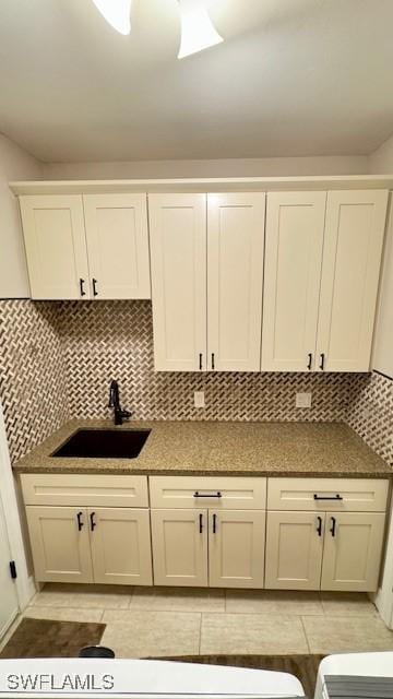 kitchen featuring decorative backsplash, light tile patterned floors, white cabinetry, and sink