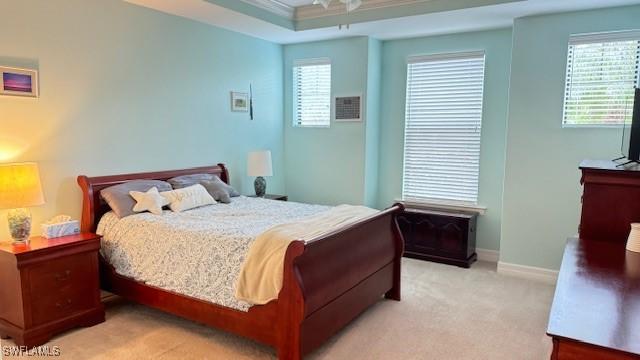 carpeted bedroom with a raised ceiling, multiple windows, and ornamental molding