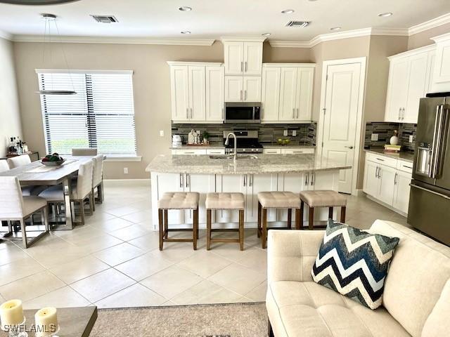 kitchen featuring backsplash, light stone counters, stainless steel appliances, a breakfast bar area, and an island with sink