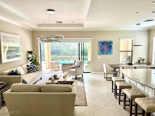 tiled living room featuring crown molding, a tray ceiling, and a chandelier