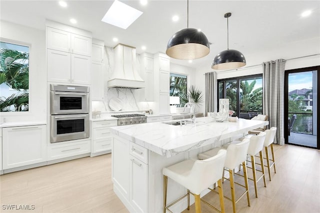 kitchen with an island with sink, custom range hood, and white cabinets