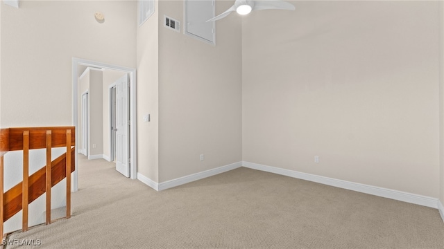 carpeted empty room featuring ceiling fan and a towering ceiling