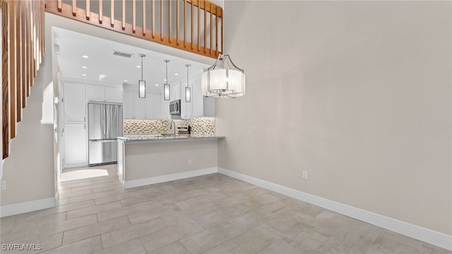 kitchen featuring kitchen peninsula, backsplash, stainless steel appliances, white cabinetry, and hanging light fixtures