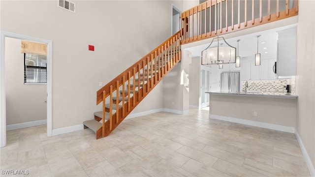 stairway with a notable chandelier, sink, and a high ceiling