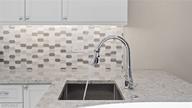 interior details featuring light stone counters, white cabinetry, tasteful backsplash, and sink