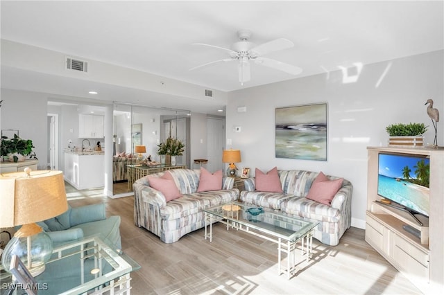 living room with light hardwood / wood-style flooring, ceiling fan, and sink