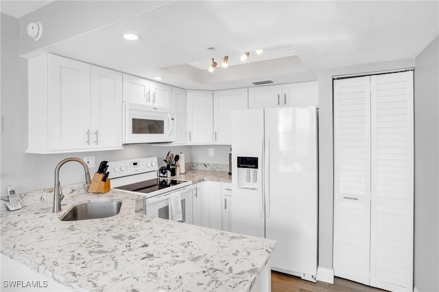 kitchen with a peninsula, white appliances, white cabinetry, and a sink