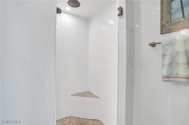 bathroom with a textured wall and a tile shower