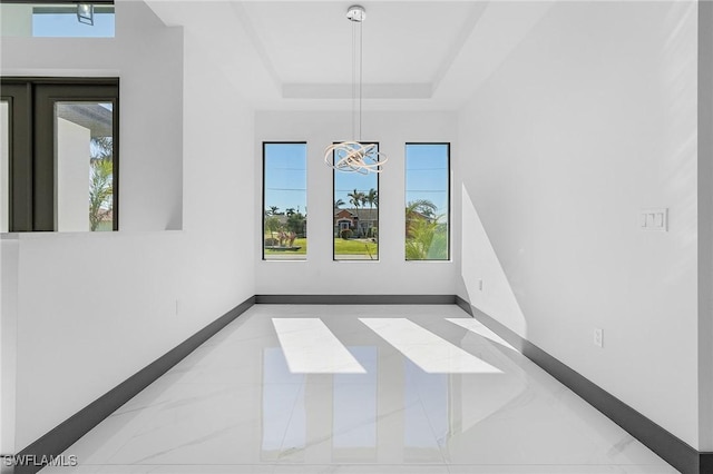 empty room featuring a raised ceiling and a notable chandelier