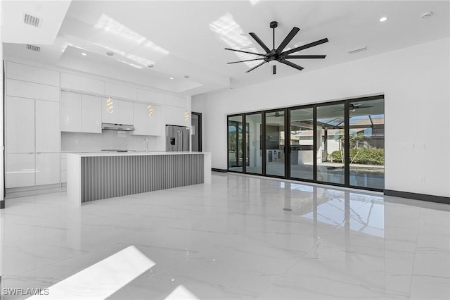 kitchen featuring stainless steel refrigerator with ice dispenser, a raised ceiling, ceiling fan, white cabinets, and an island with sink