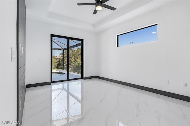 empty room with ceiling fan and a tray ceiling