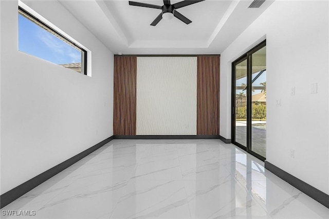 empty room featuring ceiling fan, a wealth of natural light, and a tray ceiling