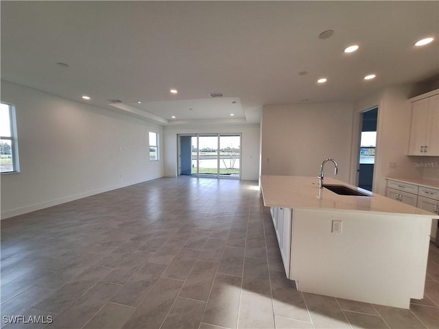 kitchen featuring white cabinetry, sink, tile patterned flooring, a kitchen island with sink, and a raised ceiling