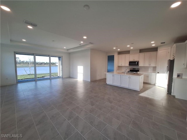 kitchen featuring appliances with stainless steel finishes, sink, a water view, a center island with sink, and white cabinetry