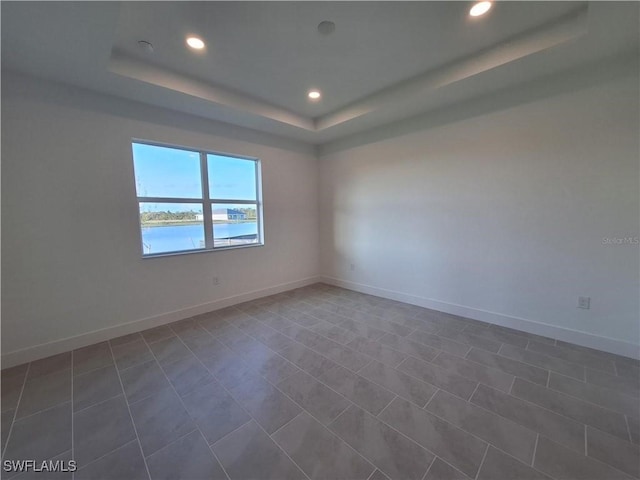 tiled spare room with a raised ceiling and a water view