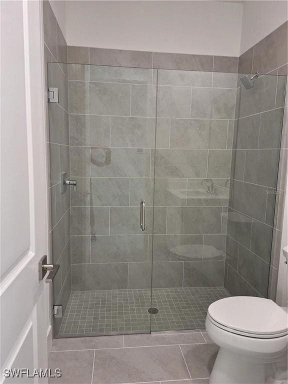 bathroom with tile patterned floors, a shower with shower door, and toilet